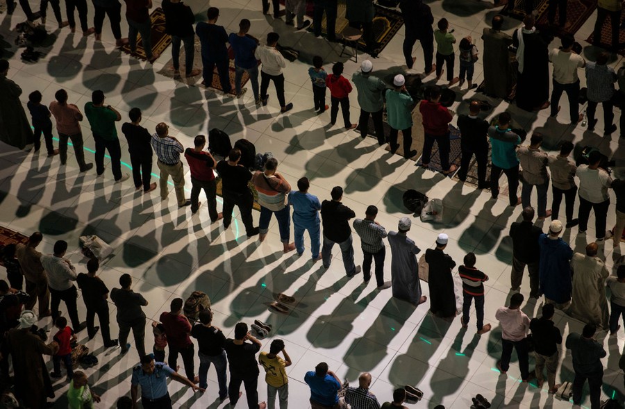 Dozens of men stand in rows, side by side, in prayer.