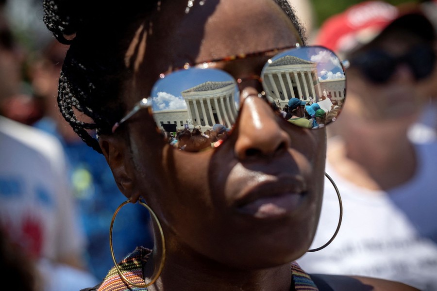 The U.S. Supreme Court building is reflected in a person's glasses.