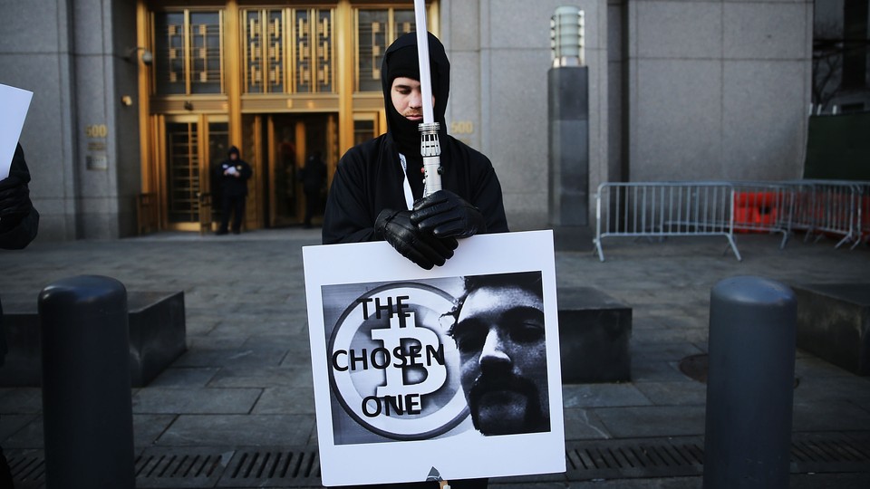 A man dressed in black holds a sign with a symbol for bitcoin