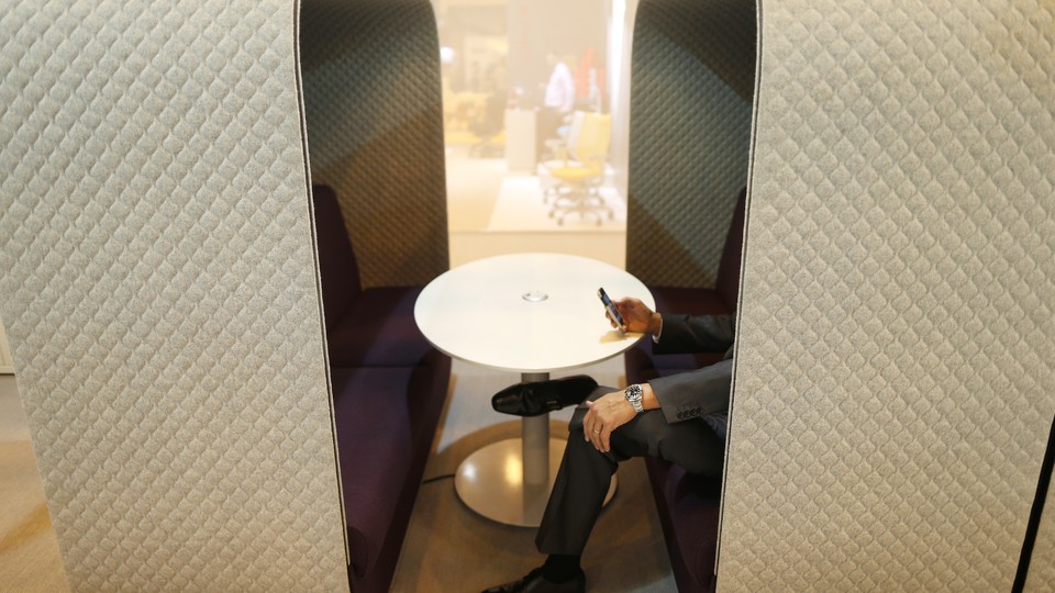 A person sits at a bench surrounded by walls on three sides and uses a smartphone in front of a round table.