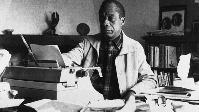 James Baldwin sits in an office in front of a typewriter