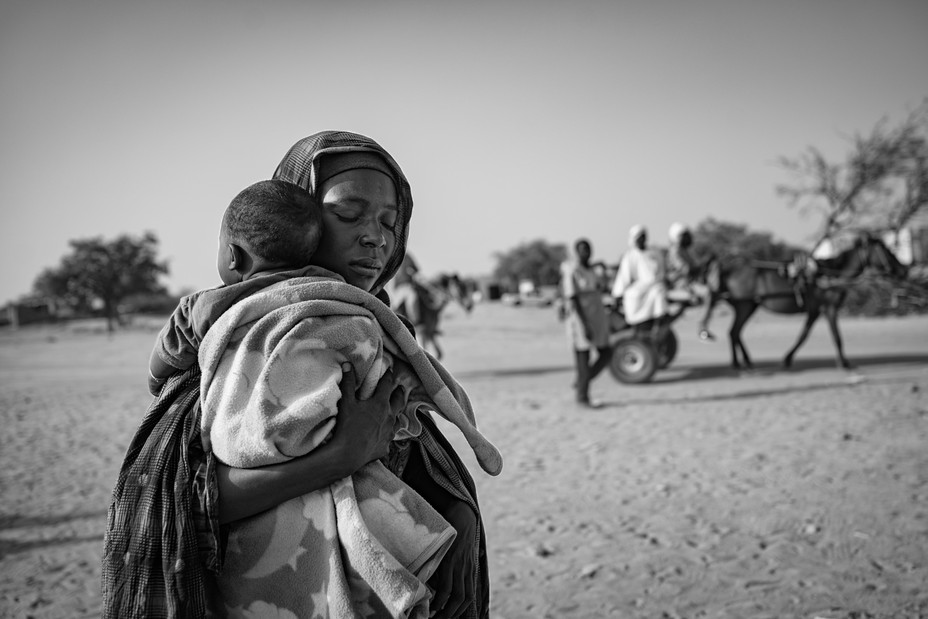 Picture of a refugee from the Zamzam camp carries her child as she arrives at the Tiné crossing into Chad.