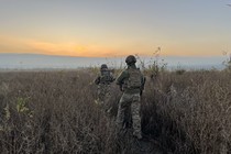 Two soldiers walk in a field at sunrise