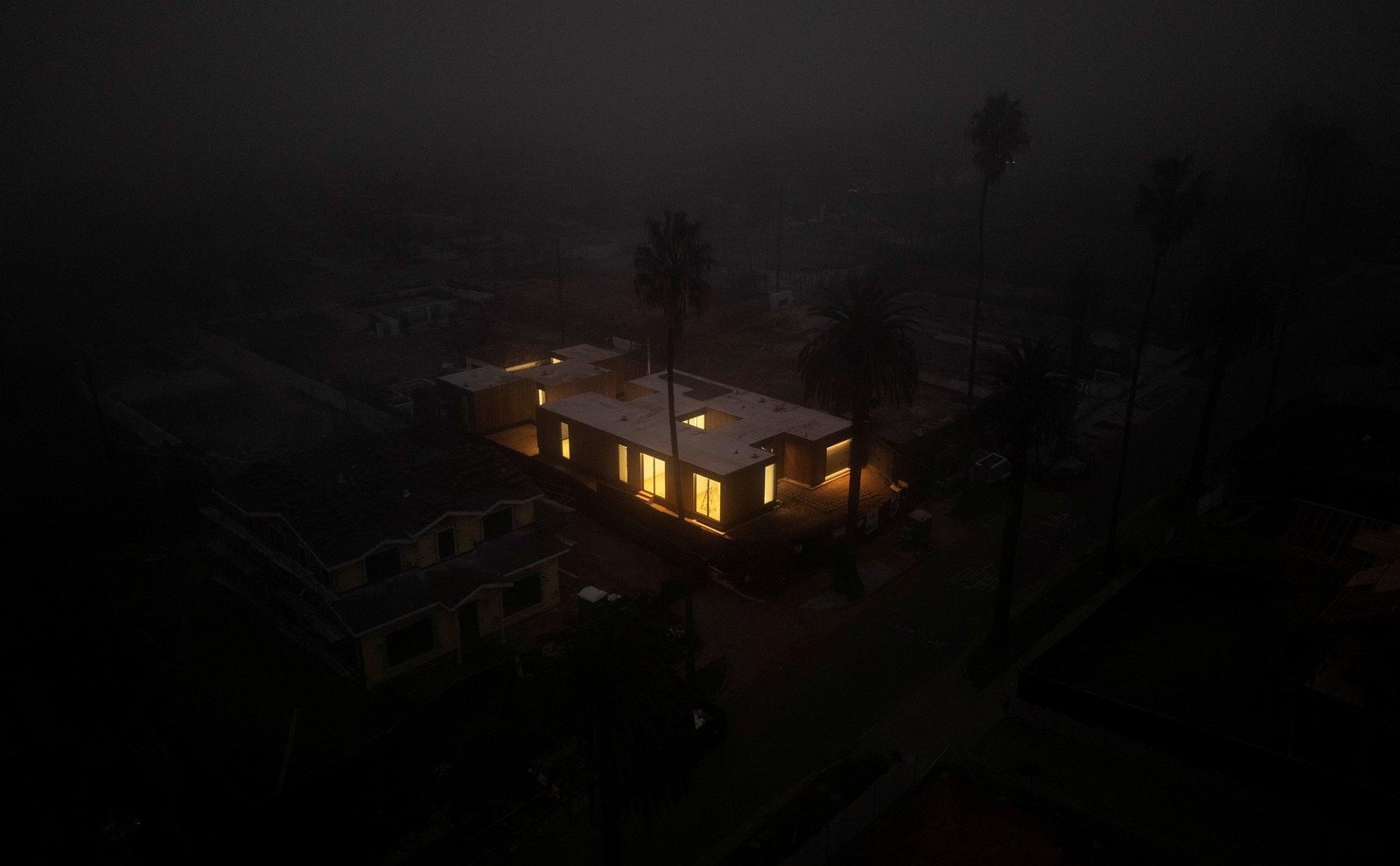 An aerial view, on a dark foggy night, of a house under construction, lit from within