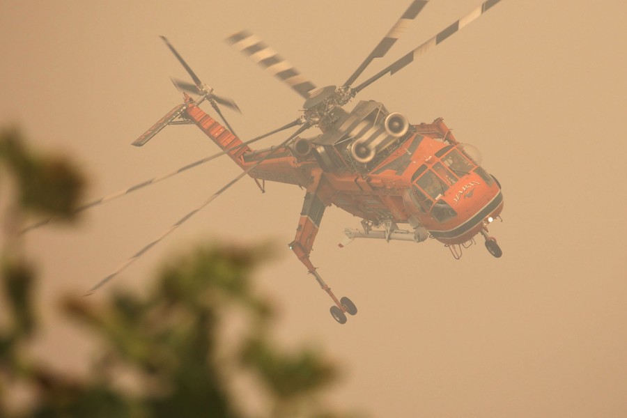 A firefighting helicopter flies through a smoky sky.