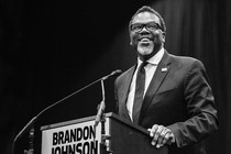 Brandon Johnson grinning as he stands behind a lectern.