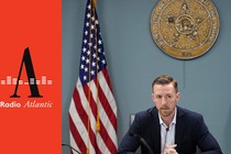 Oklahoma State Superintendent Ryan Walters sits at a table with an American flag and the state flag of Oklahoma.