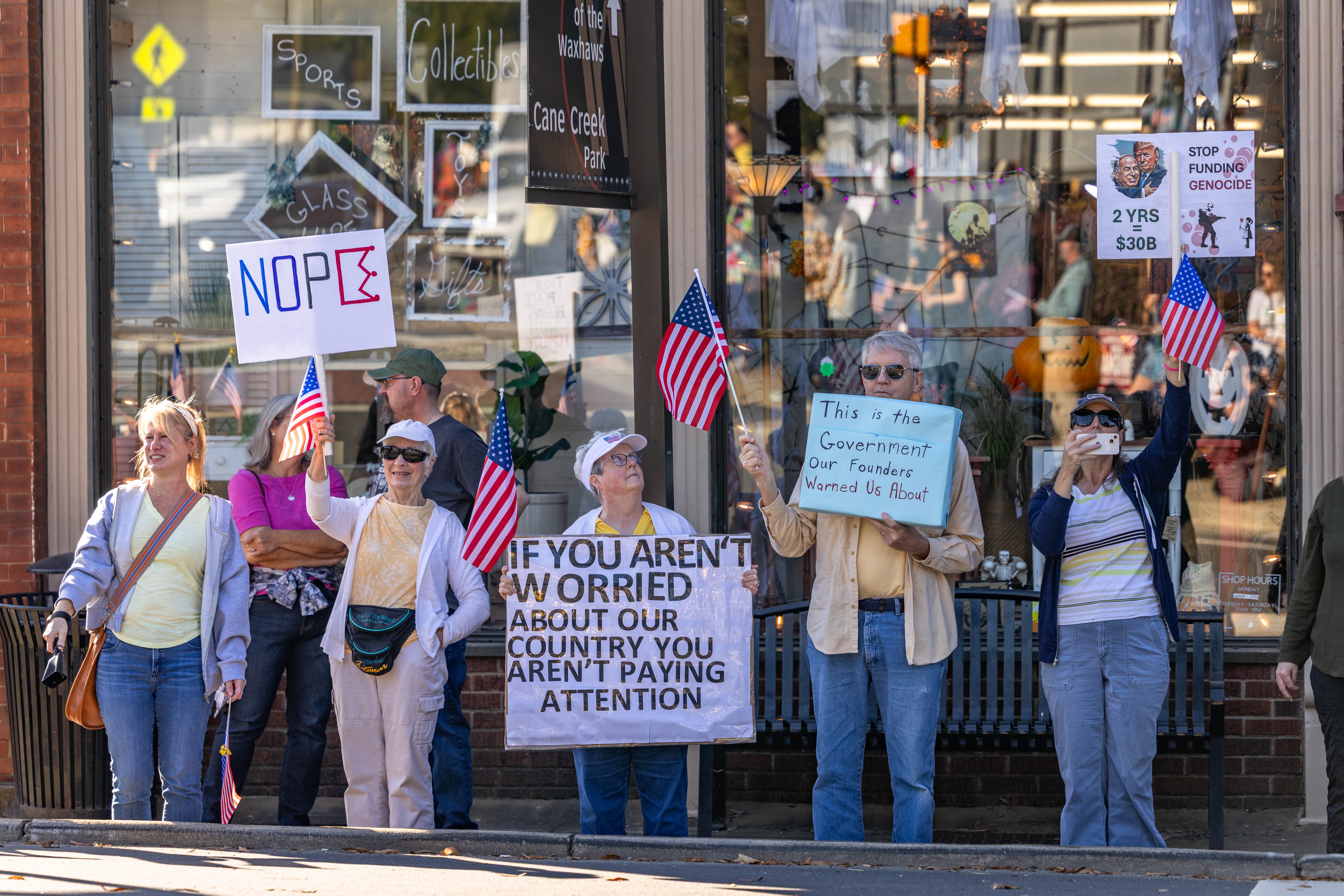 A group of protesters, hold signs, including one that reads