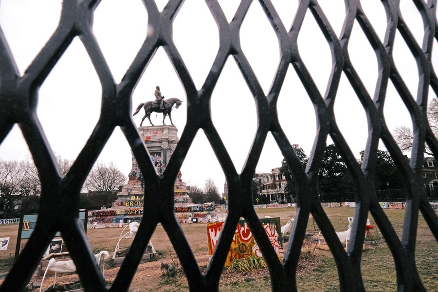 A graffiti-covered monument of Robert E. Lee is viewed through holes in a fence.