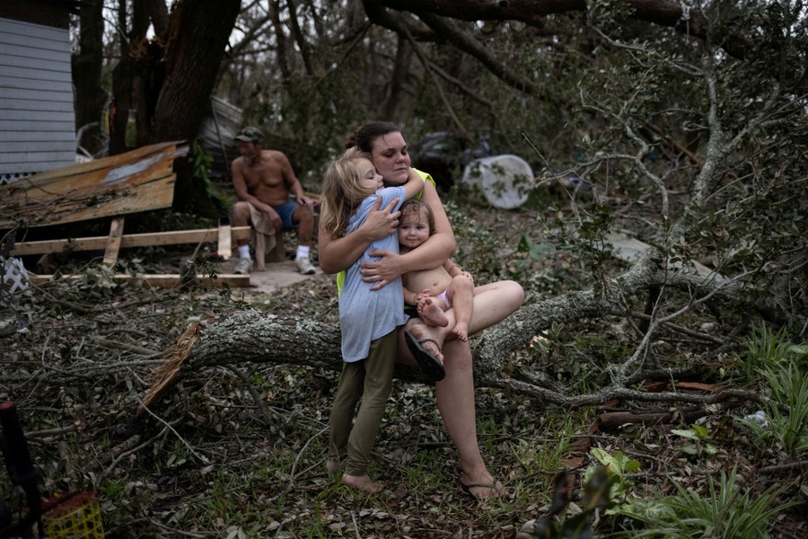 A family sits in the wreckage of trees and their home after Hurricane Ida passed.