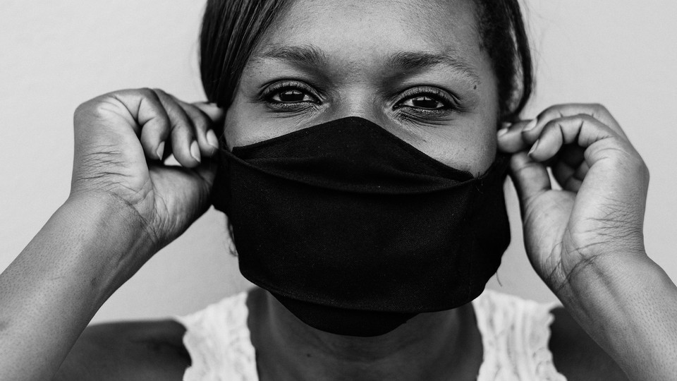 Black-and-white close-up of a woman putting on a face mask