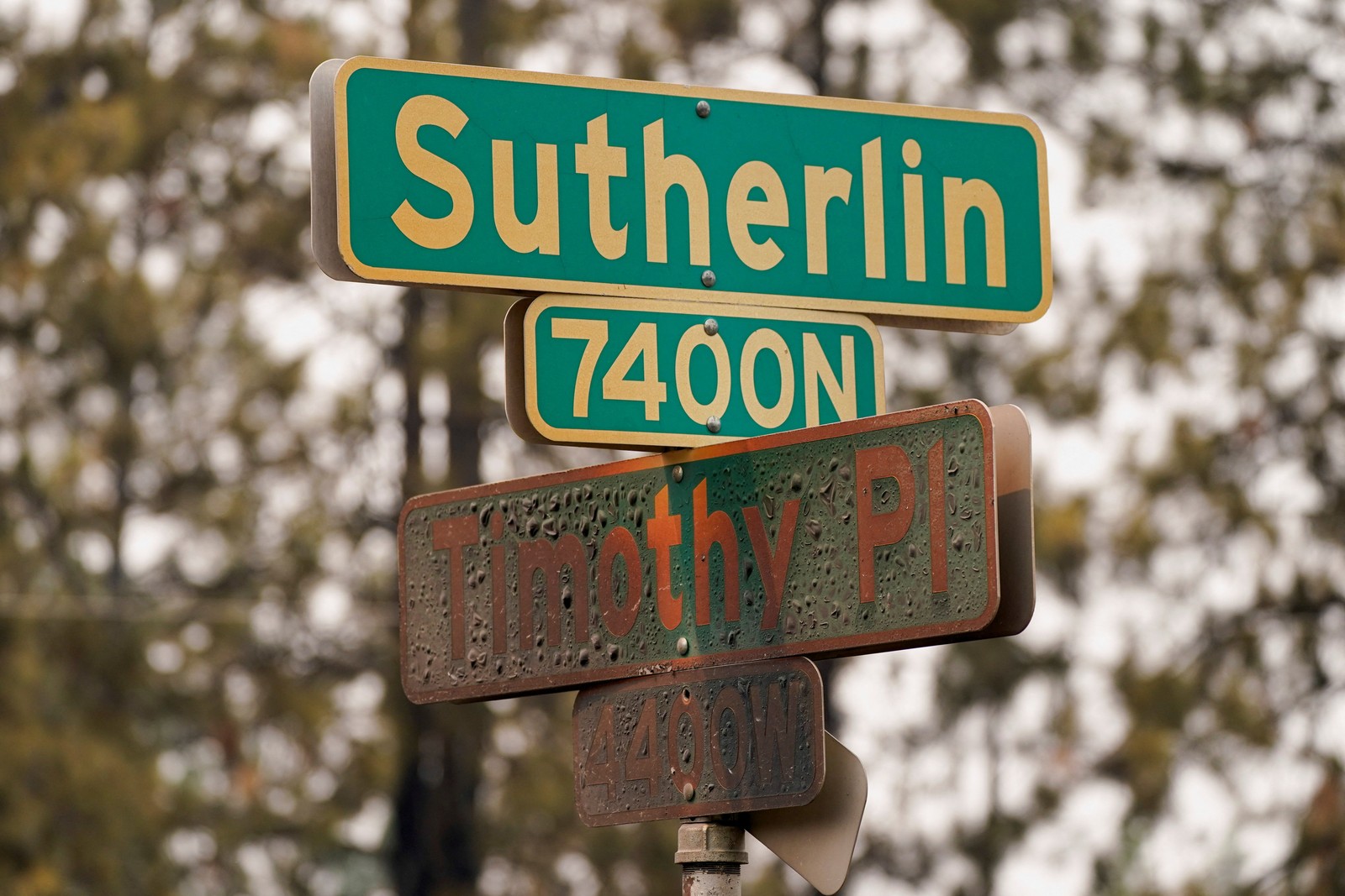 A street sign, showing two street names, Sutherlin and Timothy Place. The lower sign is badly scorched.