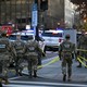 National Guardsmen in camouflage uniforms walk down a street in Washington, D.C., with yellow tape.