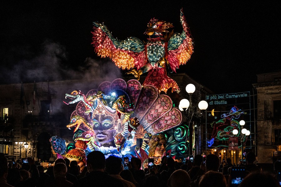 People watch as a large and colorful float passes by during a nighttime parade.