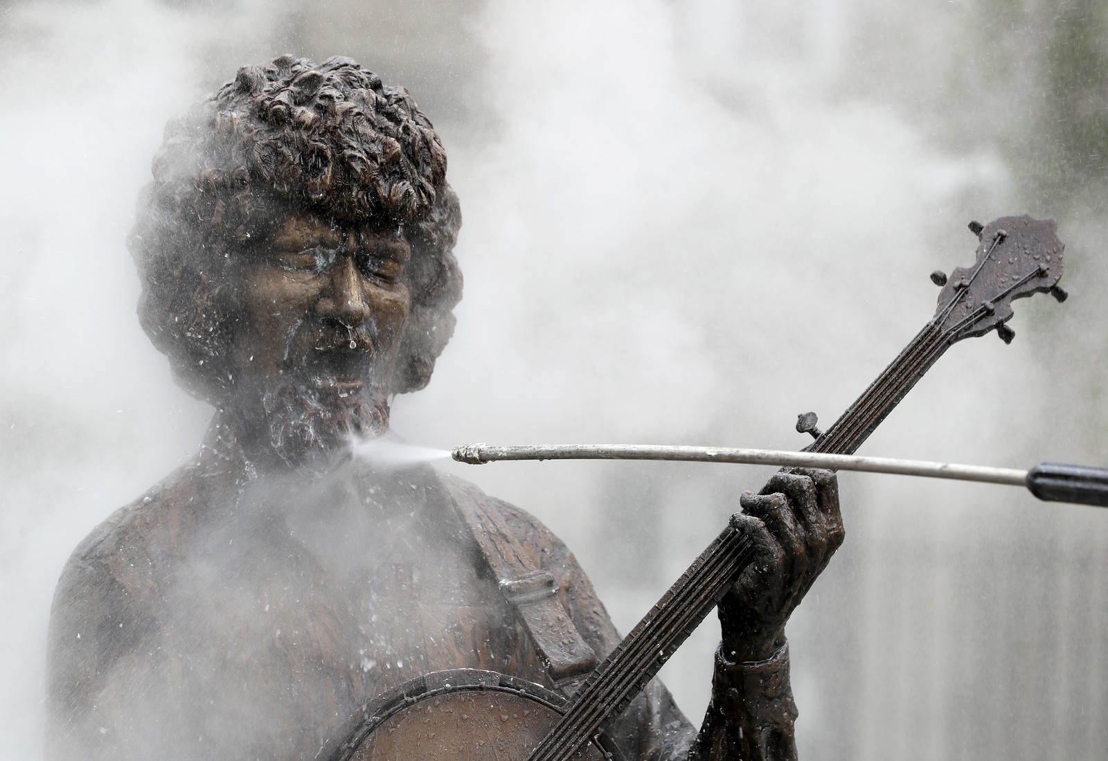 Water is sprayed from a wand onto the beard of a statue of a musician.