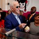 Joe Biden, in sunglasses, smiling with a spoonful of ice cream while surrounded by smiling supporters.