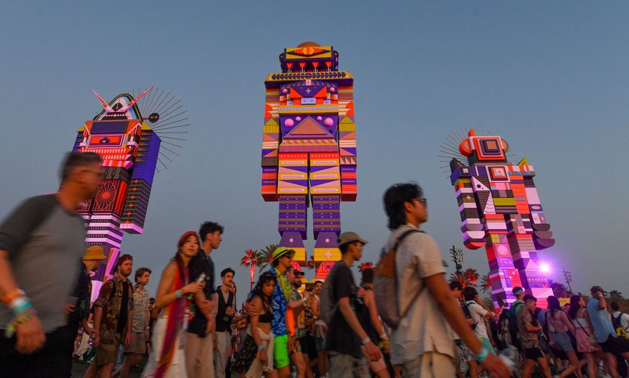 People walk past tall art installations that appear to be colorful robots.