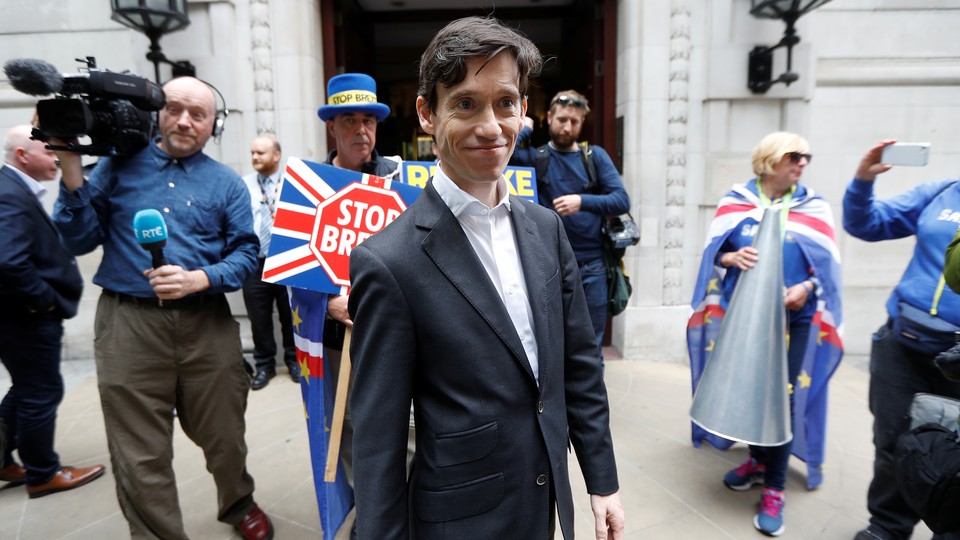 Rory Stewart emerges from TV studios in Westminster, London. A protester holding a sign reading "Stop Brexit" stands in the background.