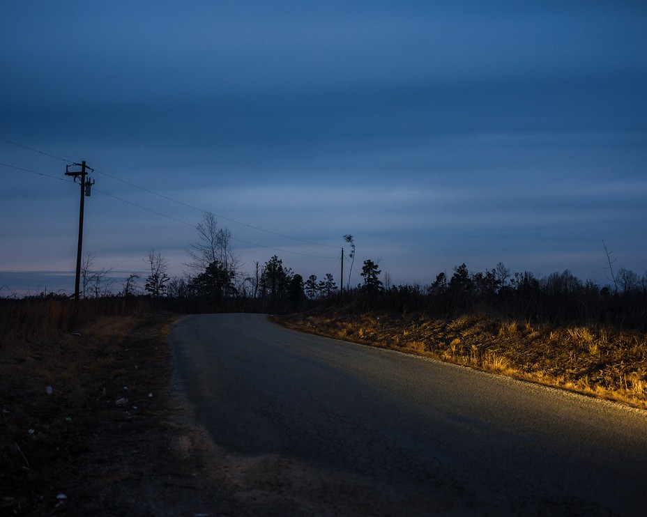 photo of darkened road partially lit by car headlights with telephone poles and wires after sunset