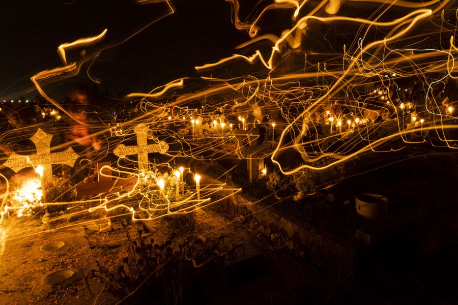 A long-exposure view of candles moving through a cemetery at night.