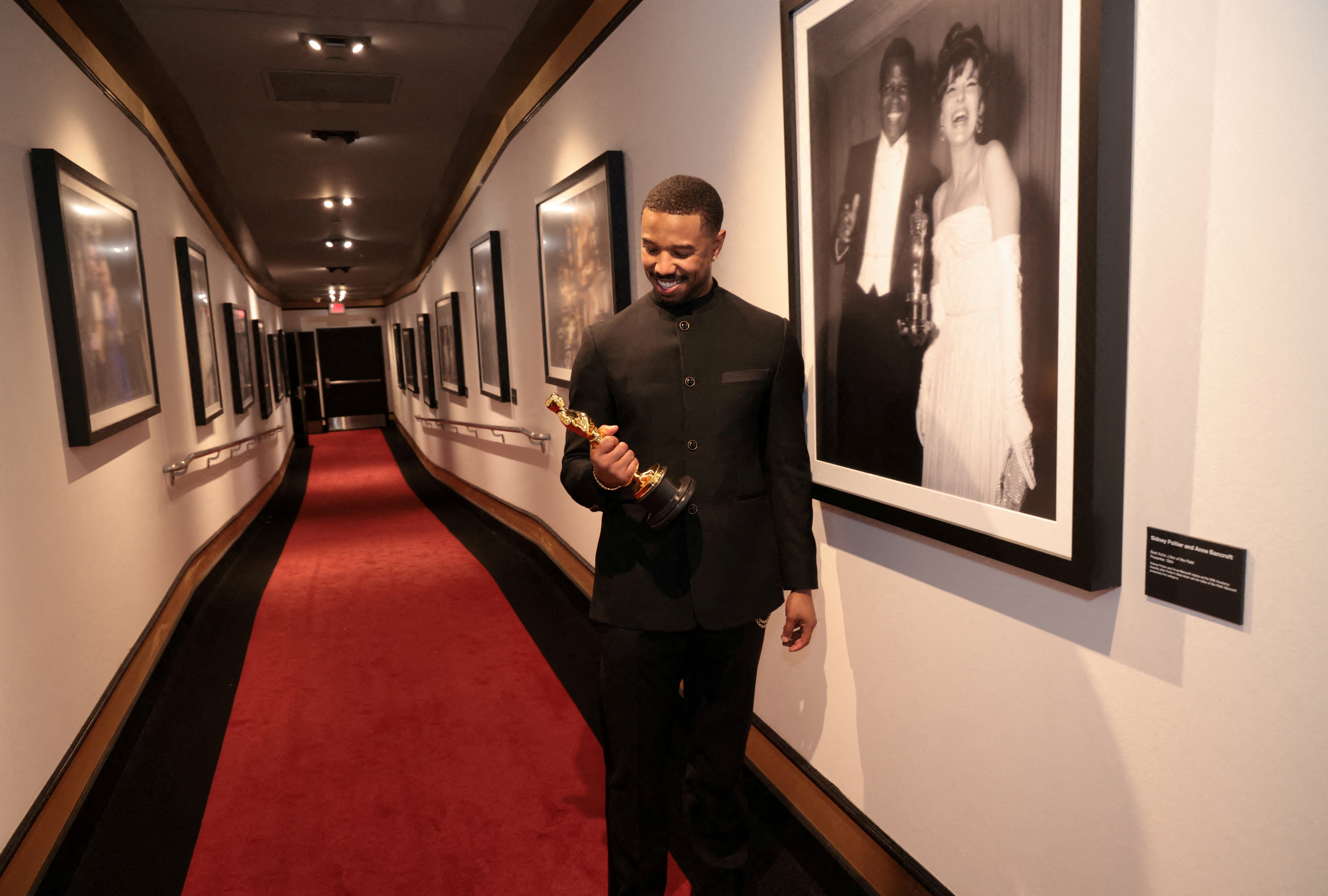 Michael B. Jordan stands in a hallway, posing with his recently-won Oscar award.