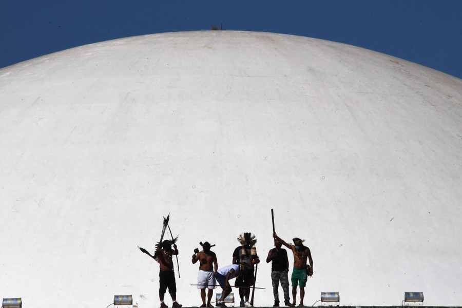 Half a dozen indigenous people protest in front of a large white dome.