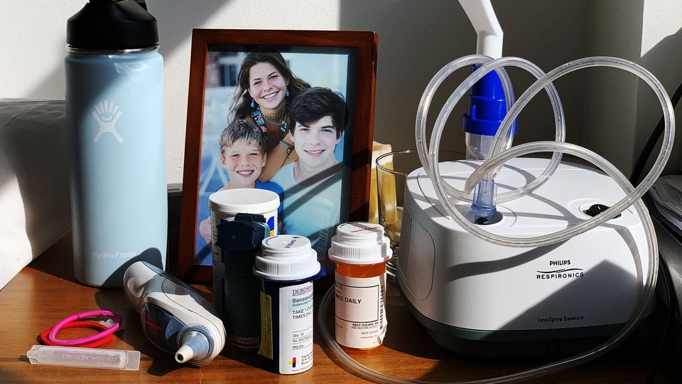 A photo of a framed family photograph, a nebulizer, a Hydro Flask, and bottles of pills on a desk