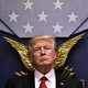Trump stands in front of a bronze eagle and 5 stars on a flag.