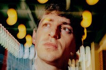 A photo of Alex Edelman surrounded by blurred lights outside of Hudson Theatre in New York
