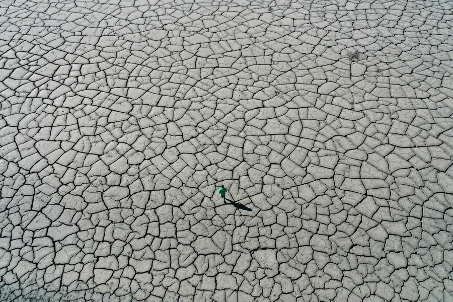 A person walks on cracked earth, the floor of a dried-up reservoir.