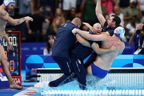 Coaches and a member of a water-polo team celebrate, embracing and falling into a pool together.