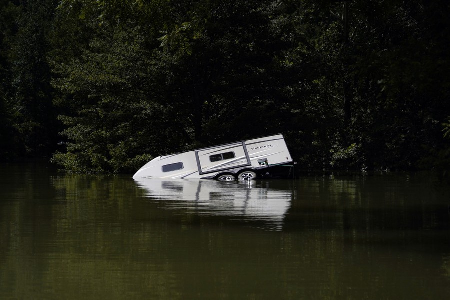 A camper sits partly submerged under floodwater.