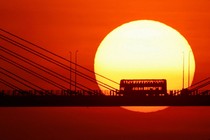 A double-decker bus passes over a bridge, silhouetted at sunset.