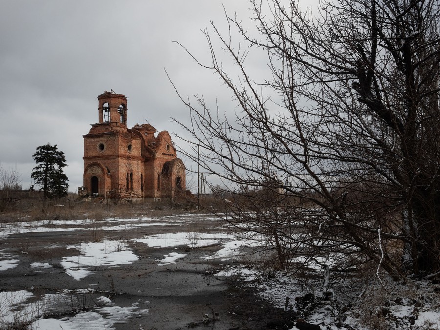Ruins of a heavily-damaged church stand in an overgrown field.