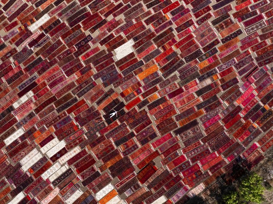 Dozens of hand-woven rugs laid on the ground outside