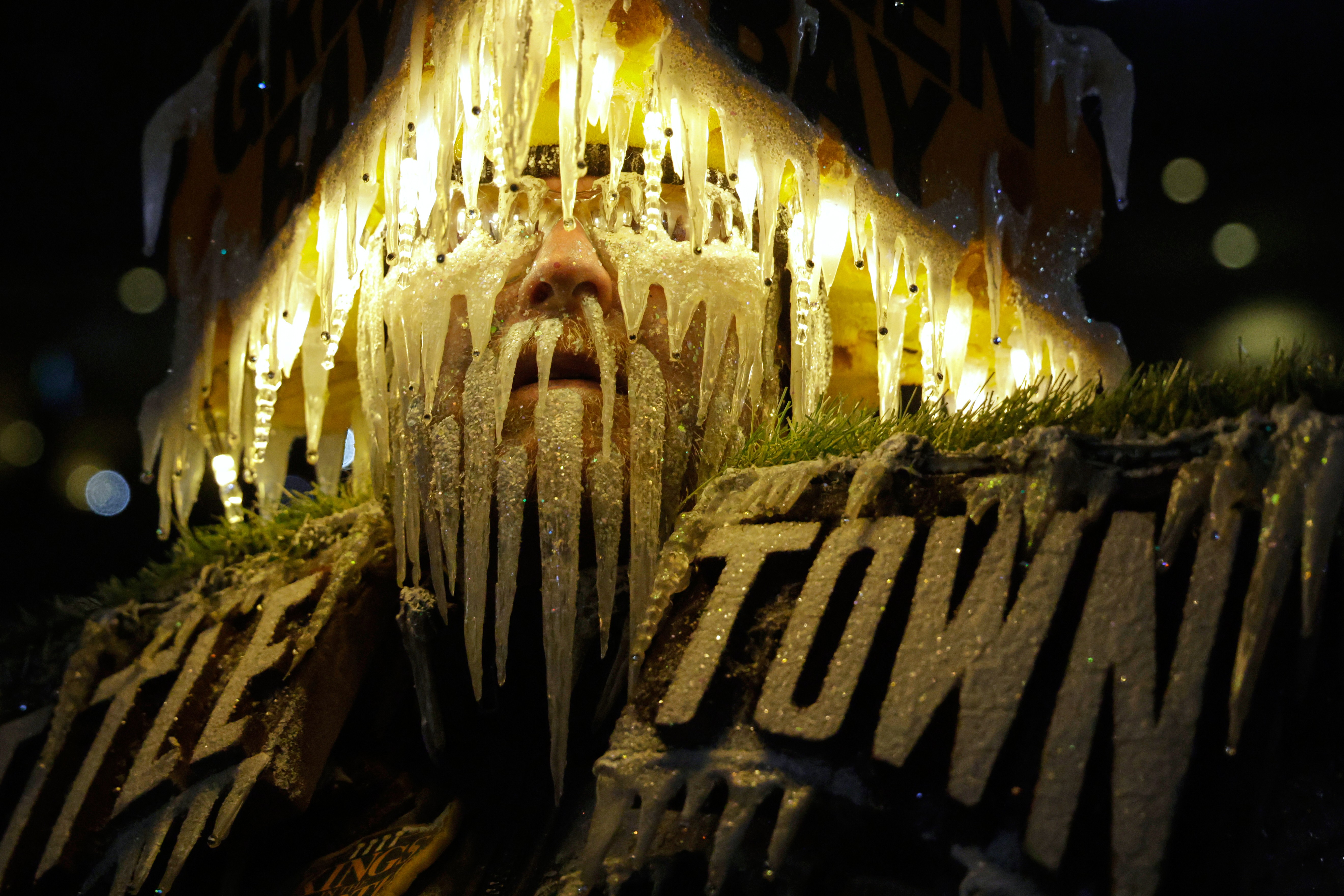 A football fan wears an elaborate costume, looking like a frozen cheesehead (with a cheese-shaped hat, illuminated icicles on hat and face)