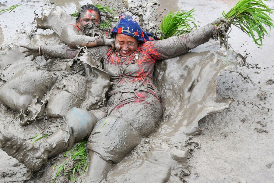 Mud-covered farmers play in a paddy field.