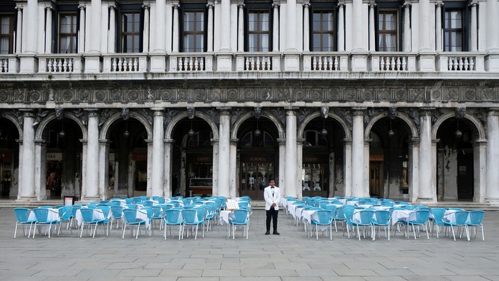 A waiter stands by empty tables outside a restaurant at St Mark's Square, which is usually full of tourists, after Italy's government adopted a decree with emergency new measures to contain the coronavirus