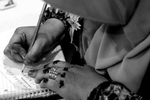 A woman wearing a headscarf writes English letters on paper.