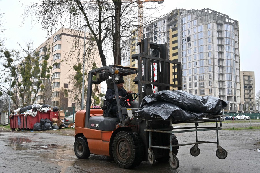 A forklift carries several body bags down a city street.