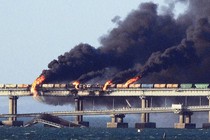 Black smoke billows from a train on a bridge.