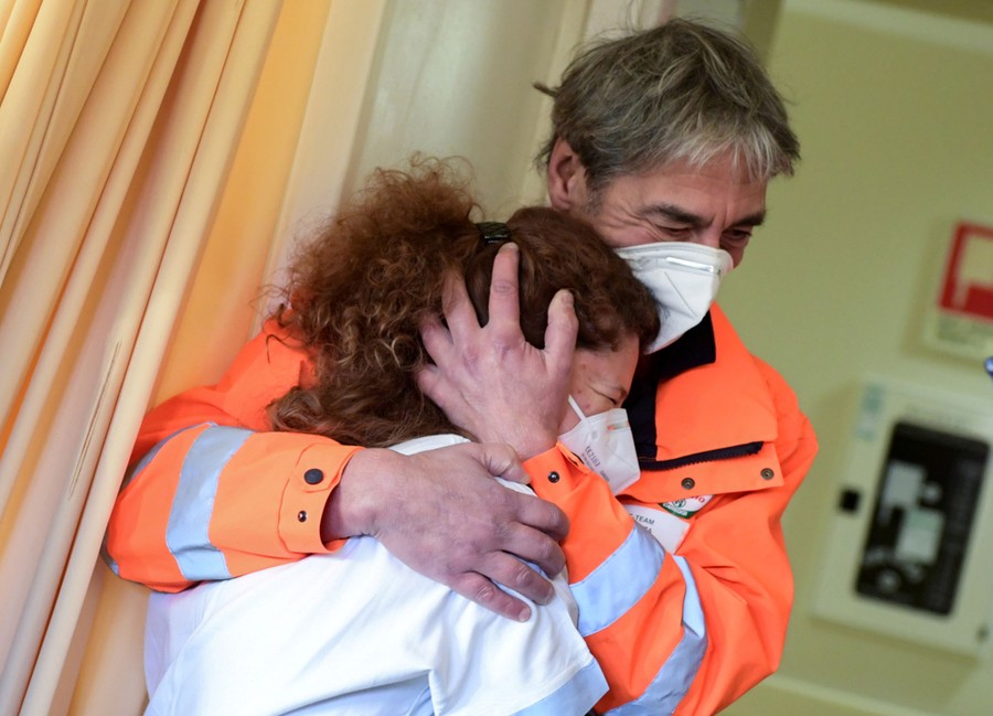 Two masked people hug inside a hospital room.