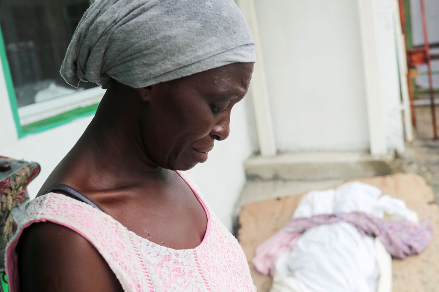 A woman looks down while standing next to the covered body of her daughter.