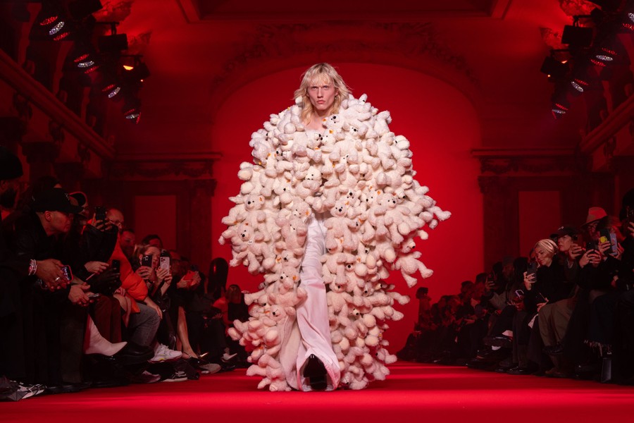 A model wearing a long coat made of stuffed animals walks down a runway.