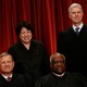 Supreme Court justices stand in front of a red backdrop. 