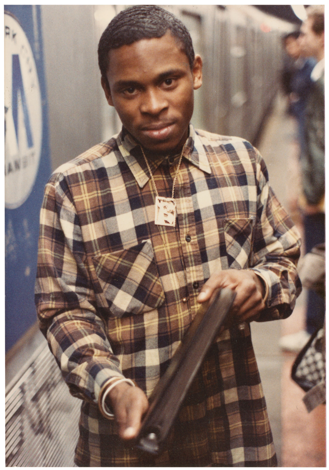 photo of man in brown plaid shirt holding photo album next to subway train