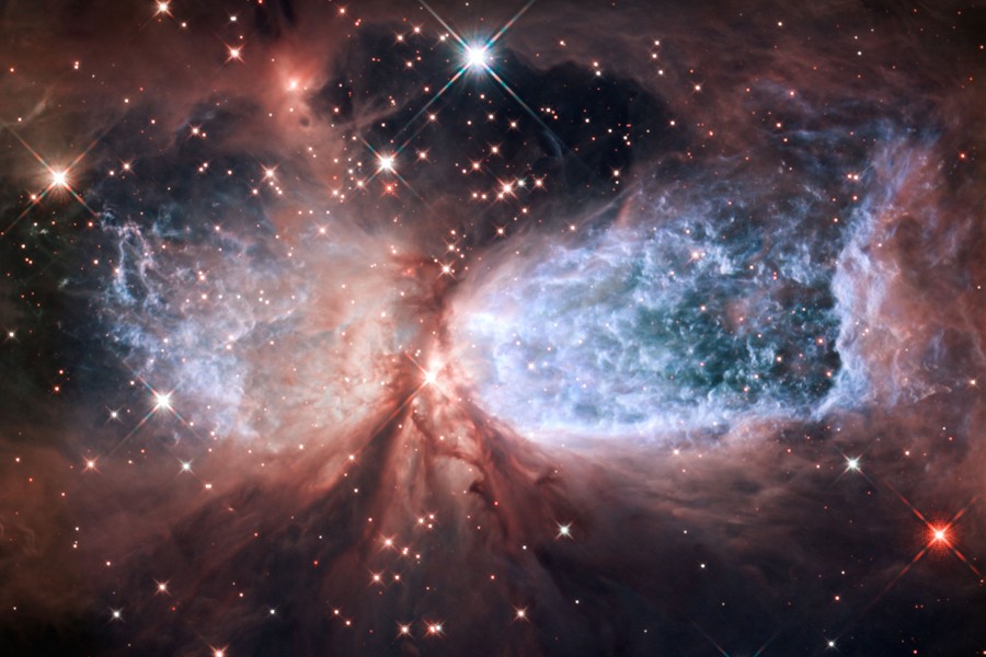 Gas, dust, and starlight form a glowing explosion, vaguely shaped like an hourglass lying on its side.