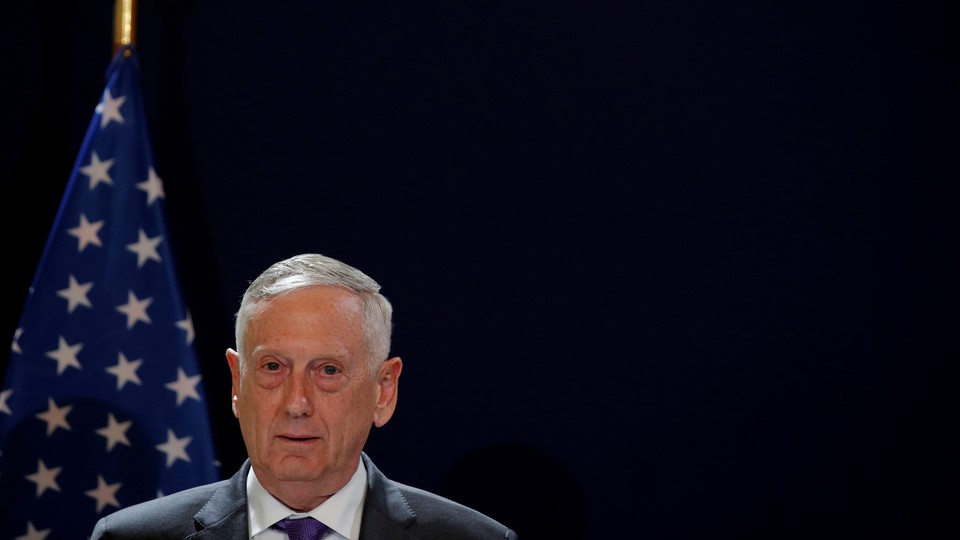 James Mattis stands in front of a black background and an American flag.