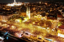 A drone view of a large crowd gathering to celebrate alongside the River Danube in Budapest, at night.