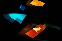 fragments of bright color against a black background; one of them has a silhouette of a hand within it